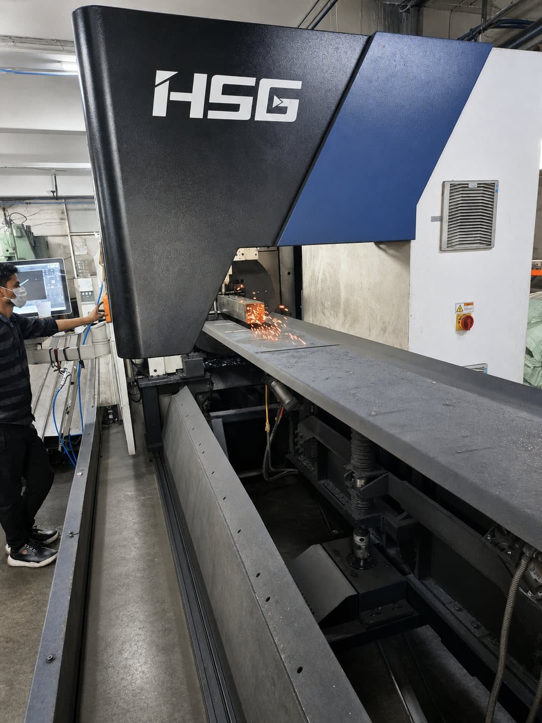 Fibre laser cutting a square steel tube, sparks at the cut, operator at the control screen