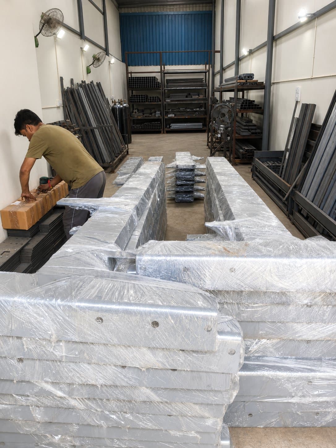 Stacks of galvanised platform sections shrink-wrapped for dispatch in the warehouse, a worker packing boxes beside them