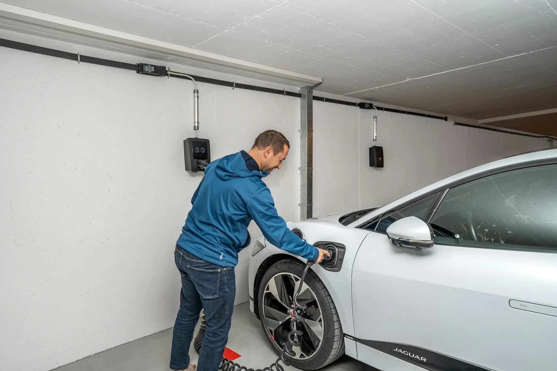 Driver connecting an electric car to a wall-mounted charger in a shared garage