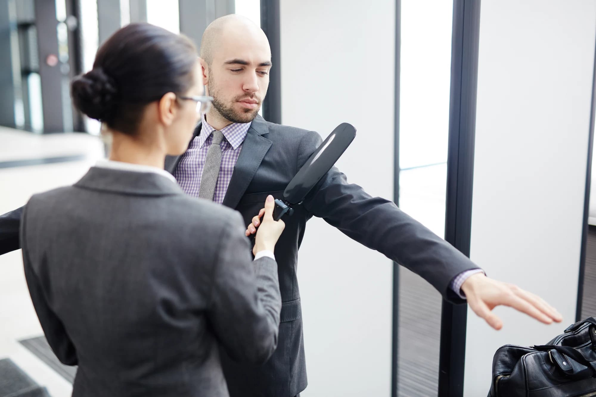 Security officer checking a visitor with a handheld metal detector