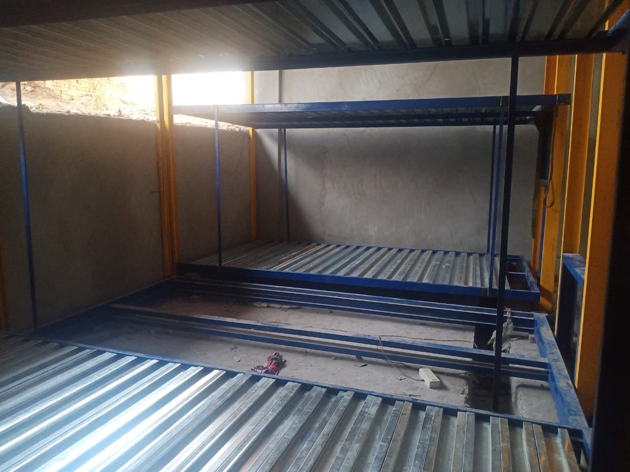 Two-level pit parking frame under construction with galvanised platforms and yellow columns inside a concrete pit