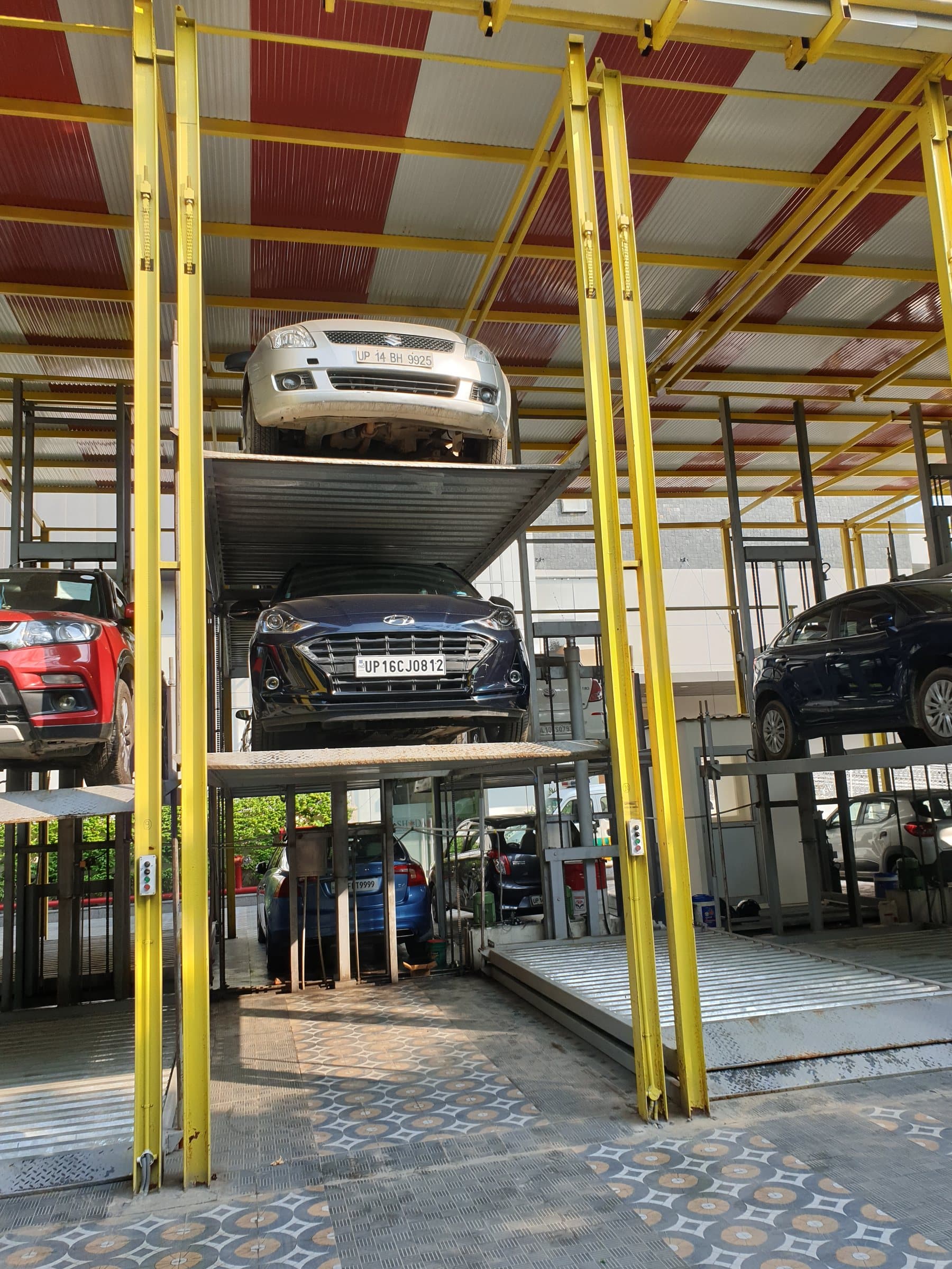 Three cars stacked vertically on a three-level hydraulic stack parking unit with yellow posts under a red and white roof